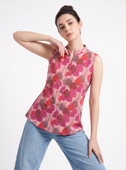 A woman modeling a sleeveless, mandarin-collar blouse with a pink, red, and brown leaf pattern, paired with light blue jeans, against a plain white studio background.