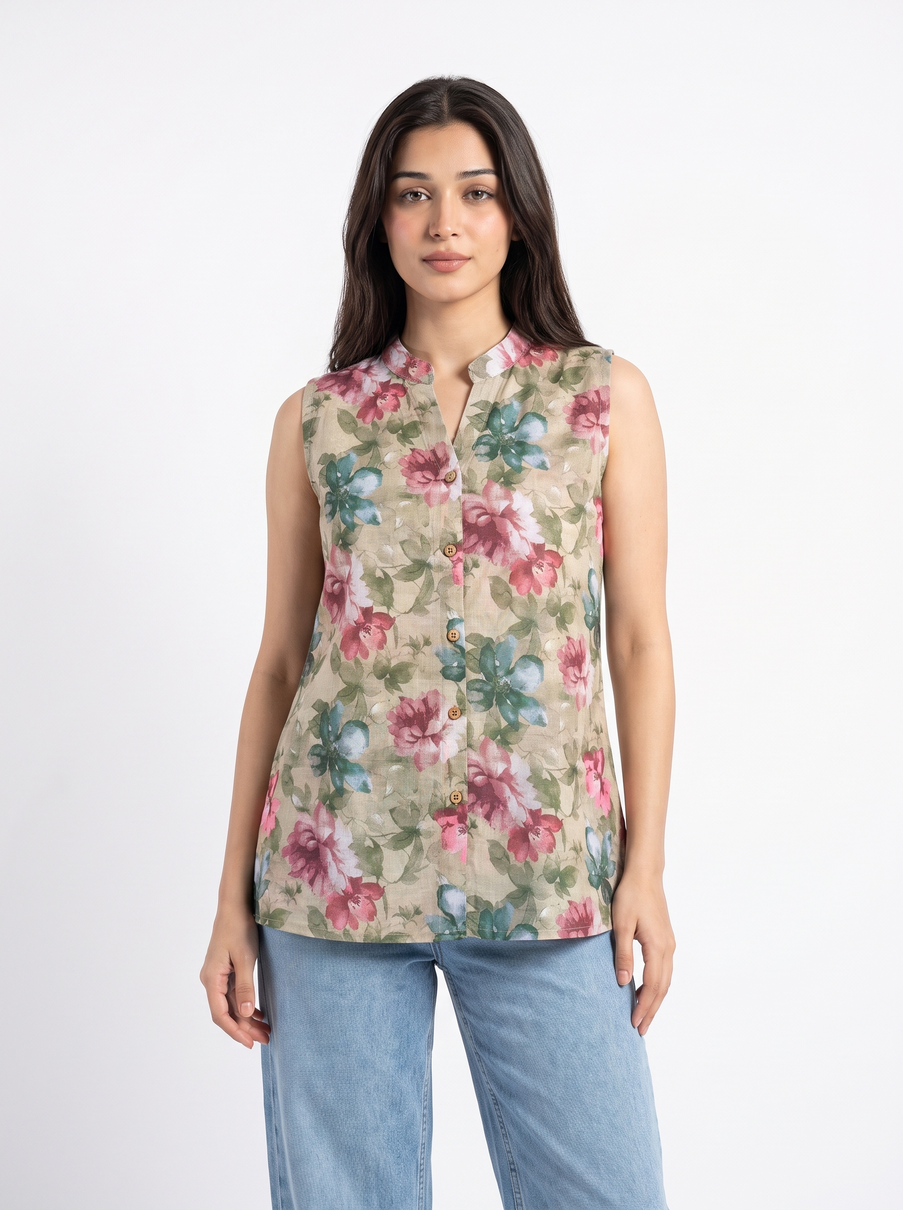 A woman modeling a sleeveless beige button-up blouse with a pink and green floral print, paired with light blue jeans, against a plain white studio background.