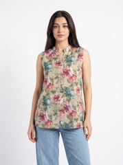 A woman modeling a sleeveless beige button-up blouse with a pink and green floral print, paired with light blue jeans, against a plain white studio background.
