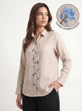 Woman wearing a beige shirt with blue floral embroidery, inset showing embroidery detail.