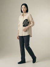 A contemporary cream shirt top featuring a bold black monstera leaf graphic on the front for a clean and artistic statement look.