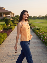 A woman walking on a stone path at a golf resort, wearing a light orange and white vertically striped sleeveless top with dark blue jeans.