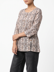 A woman wearing a three-quarter sleeve button-front top with an intricate beige, brown, and gray geometric pattern, paired with dark gray jeans, against a plain white background.