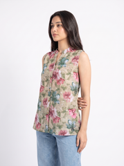 A woman modeling a sleeveless beige vest with a colorful floral print in pink, blue, and green, paired with light blue jeans, against a plain white background.