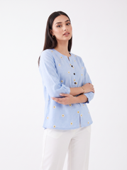 Add a fresh and feminine touch to your everyday wardrobe with this sky blue top, featuring delicate white daisy embroidery with mustard centres scattered across the front, a subtle split neckline, and contrast button detailing