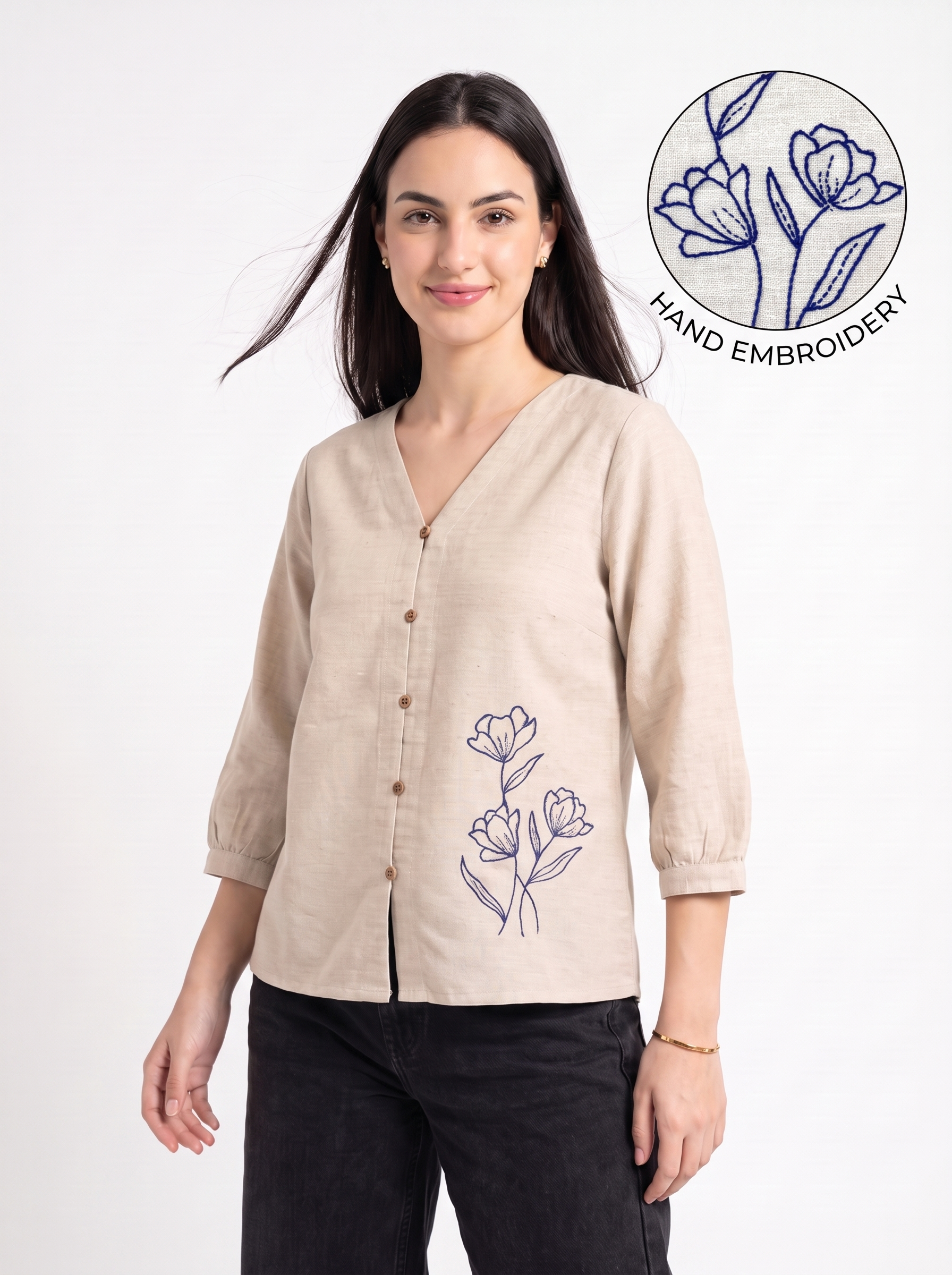 A woman modeling a beige linen button-up shirt with a V-neck and blue floral embroidery on the lower front. The image features a 'HAND EMBROIDERY' graphic overlay in the top right corner, set against a clean white background.