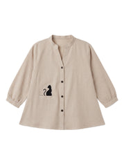 A beige long-sleeve linen button-up shirt with a stand collar, featuring a black cat silhouette graphic on the chest pocket and matching black buttons down the front.