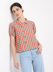 A woman wearing a short-sleeve collared button-up shirt with vertical coral red and sage green stripes, paired with light blue jeans, posing against a plain white wall.