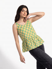 A woman modeling a sleeveless green and yellow checkered peplum top paired with black jeans, posed against a clean white studio background.