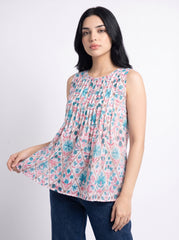 A woman modeling a sleeveless, smocked top with a pink, blue, and white geometric pattern, paired with dark blue jeans, against a plain light gray background.