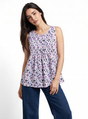 A woman modeling a sleeveless peplum top with a purple, black, and white floral print, paired with dark blue jeans, against a plain white background.