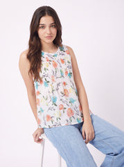 A woman wearing a sleeveless white top with a colorful floral print and light blue jeans, seated against a plain white background.