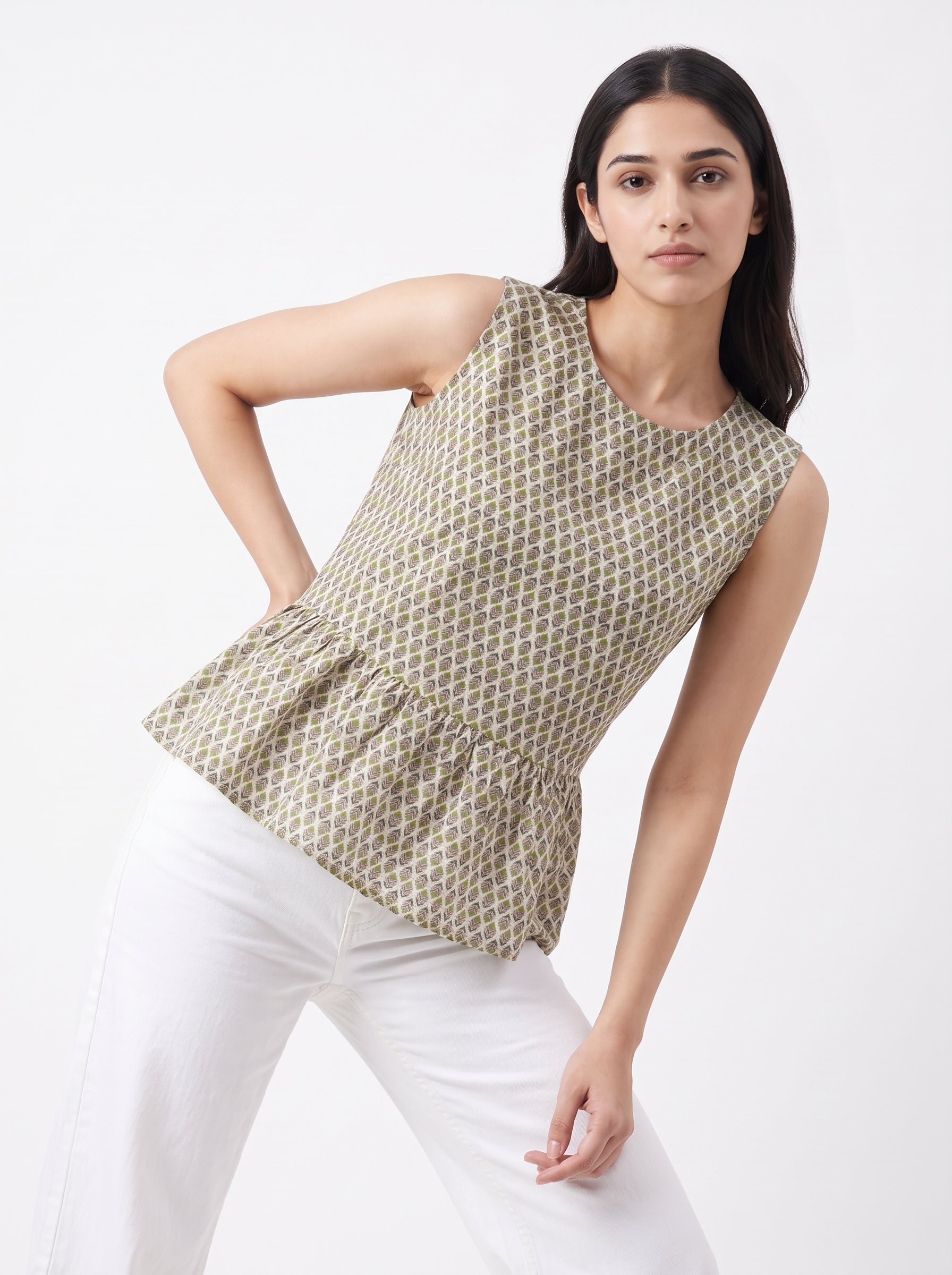 A woman modeling a sleeveless peplum top with a beige and white geometric pattern, paired with white pants, against a plain white studio background.