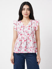 A woman modeling a white short-sleeve blouse with a pink floral print and ruffled sleeves, paired with dark blue jeans, against a light gray studio background.