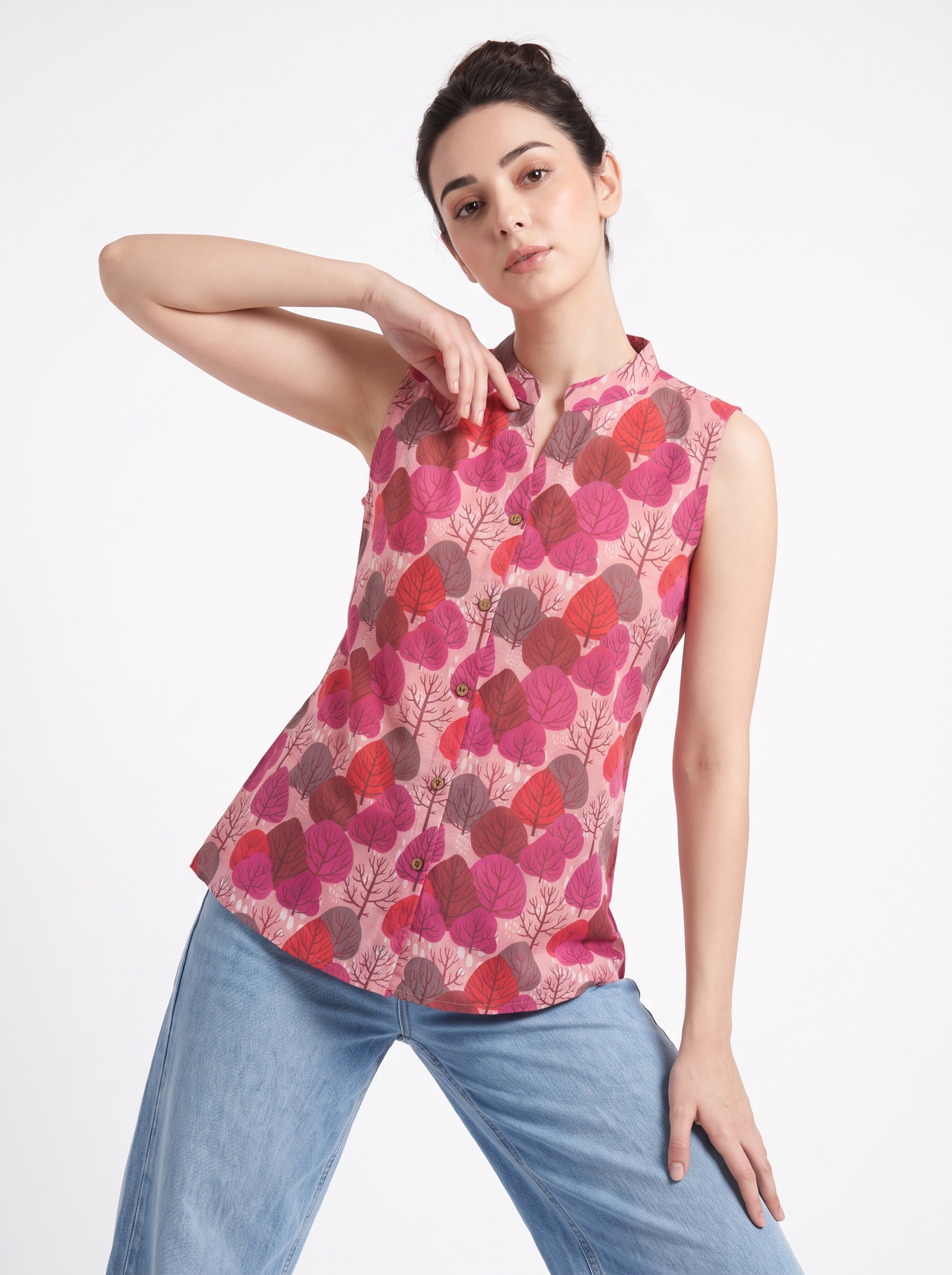 A woman modeling a sleeveless, mandarin-collar blouse with a pink, red, and brown leaf pattern, paired with light blue jeans, against a plain white studio background.