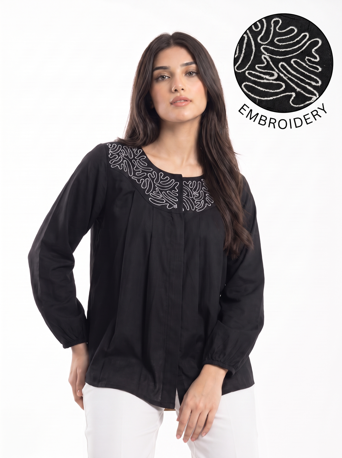 A woman wearing a black long-sleeve blouse with white floral embroidery around the neckline, paired with white pants, against a plain white background. A circular graphic in the top right shows a close-up of the white embroidery detail.