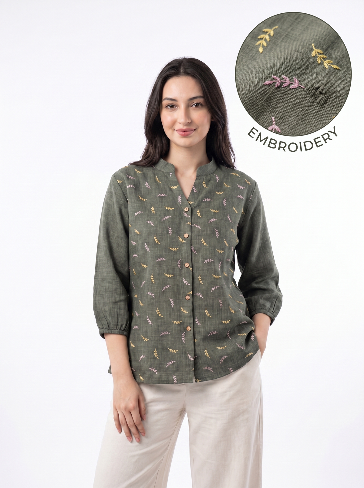 A woman modeling a sage green long-sleeve button-up shirt with a delicate multicolor embroidered pattern, paired with beige trousers. A circular inset in the top right highlights the embroidery detail.
