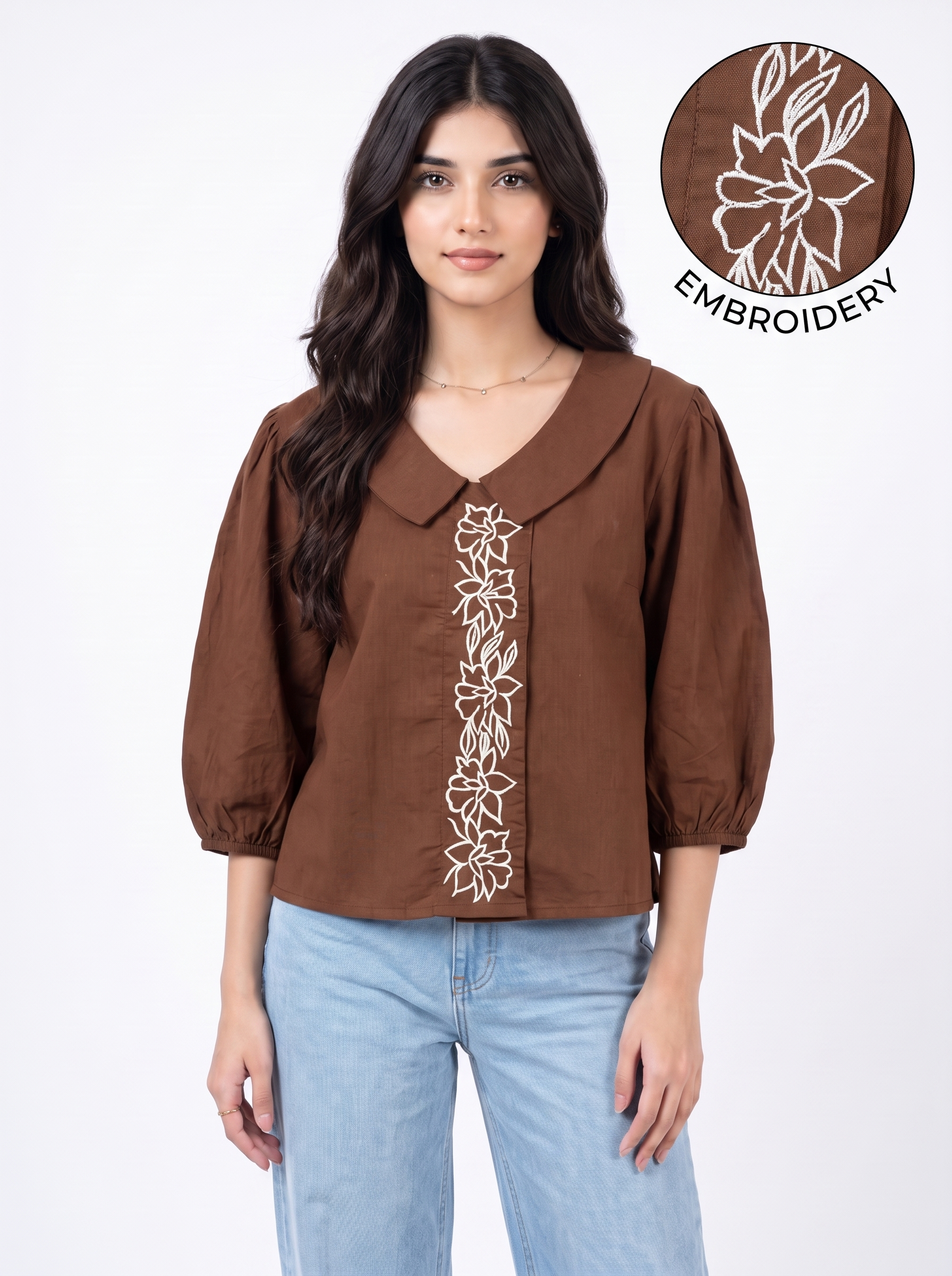 A woman wearing a brown long-sleeve blouse with white floral embroidery down the front, paired with light blue jeans. A circular inset in the top right shows a close-up of the white embroidery detail.