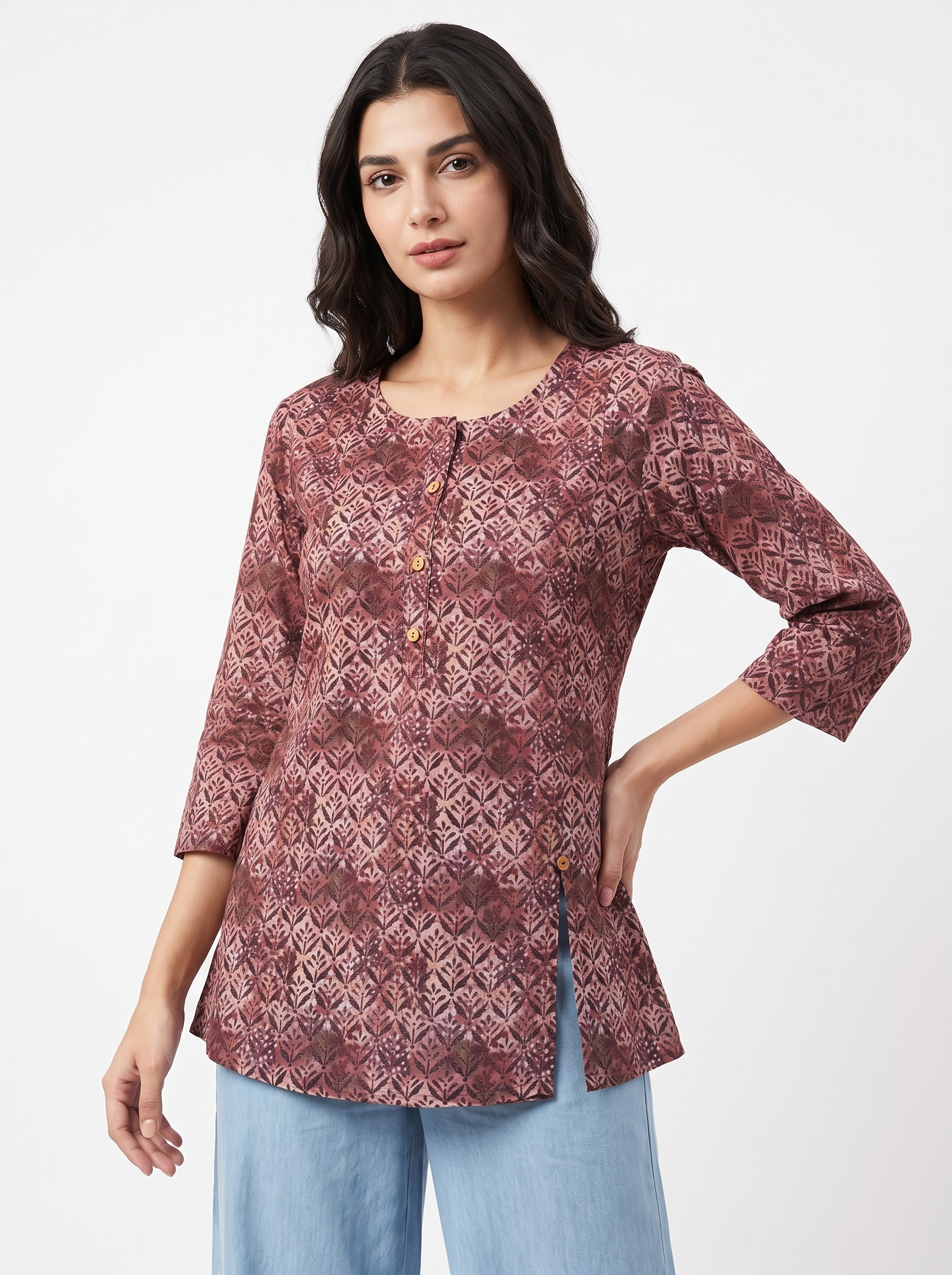 A woman modeling a three-quarter sleeve tunic top with a geometric pattern in dusty rose and burgundy, paired with light blue jeans, against a plain white studio background.