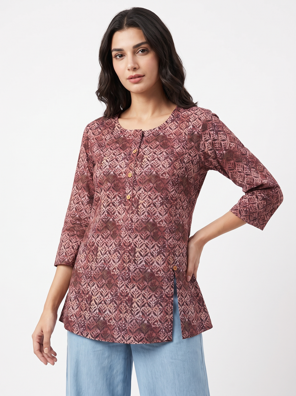 A woman modeling a three-quarter sleeve tunic top with a geometric pattern in dusty rose and burgundy, paired with light blue jeans, against a plain white studio background.