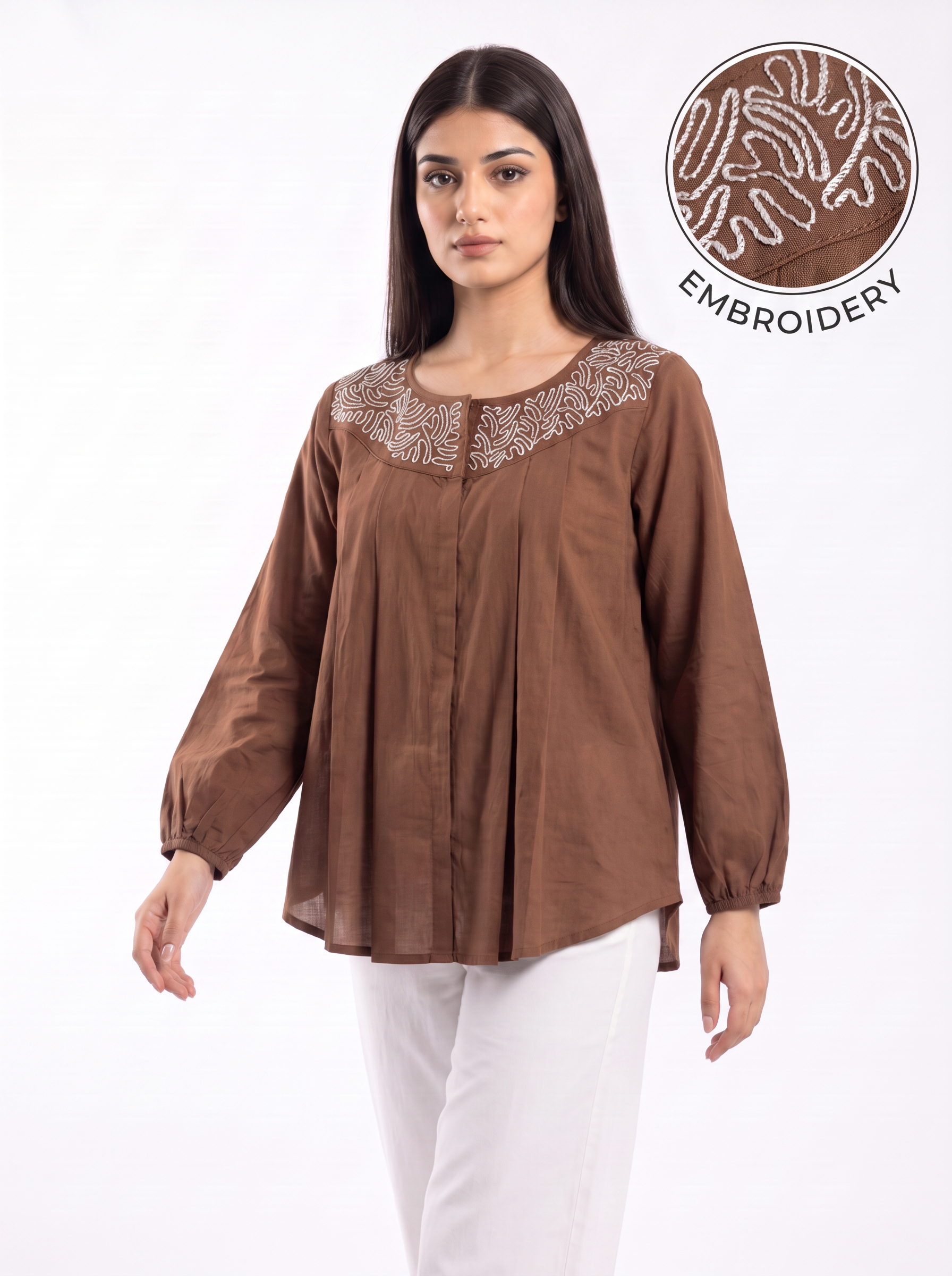 A woman modeling a brown long-sleeve top with an embroidered yoke, paired with white pants, against a plain white background. A circular inset in the top right shows a close-up of the embroidery detail.