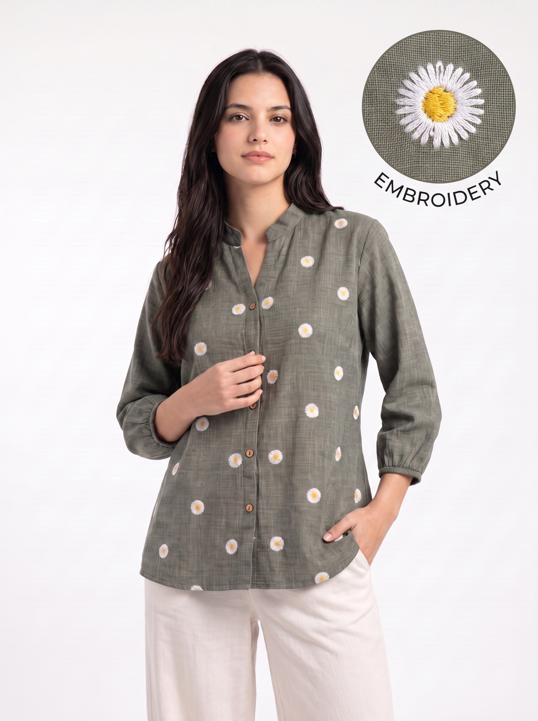 A woman wearing a sage green linen button-up shirt with white and yellow daisy embroidery, paired with off-white trousers. A circular inset in the top right shows a close-up of the daisy embroidery detail.