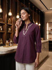 A graceful plum purple tunic top featuring delicate off-white floral vine embroidery around the neckline for an elegant handcrafted touch.