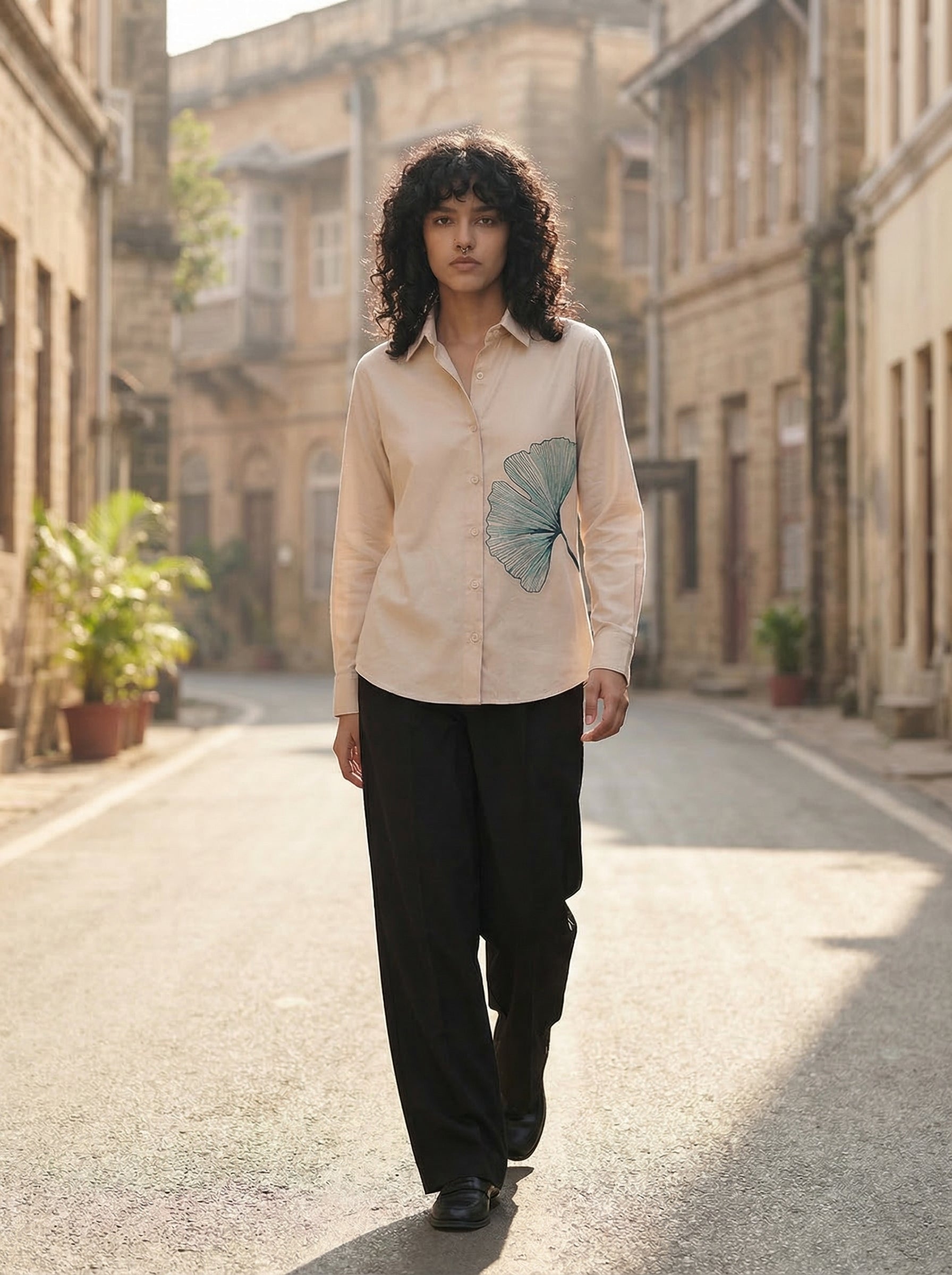 A refined cream shirt top featuring a striking teal ginkgo leaf graphic on the front for a clean artistic look.