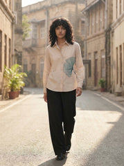 A refined cream shirt top featuring a striking teal ginkgo leaf graphic on the front for a clean artistic look.