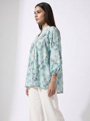 A woman modeling a light blue and white floral print blouse with three-quarter sleeves, paired with white trousers, against a plain white studio background.