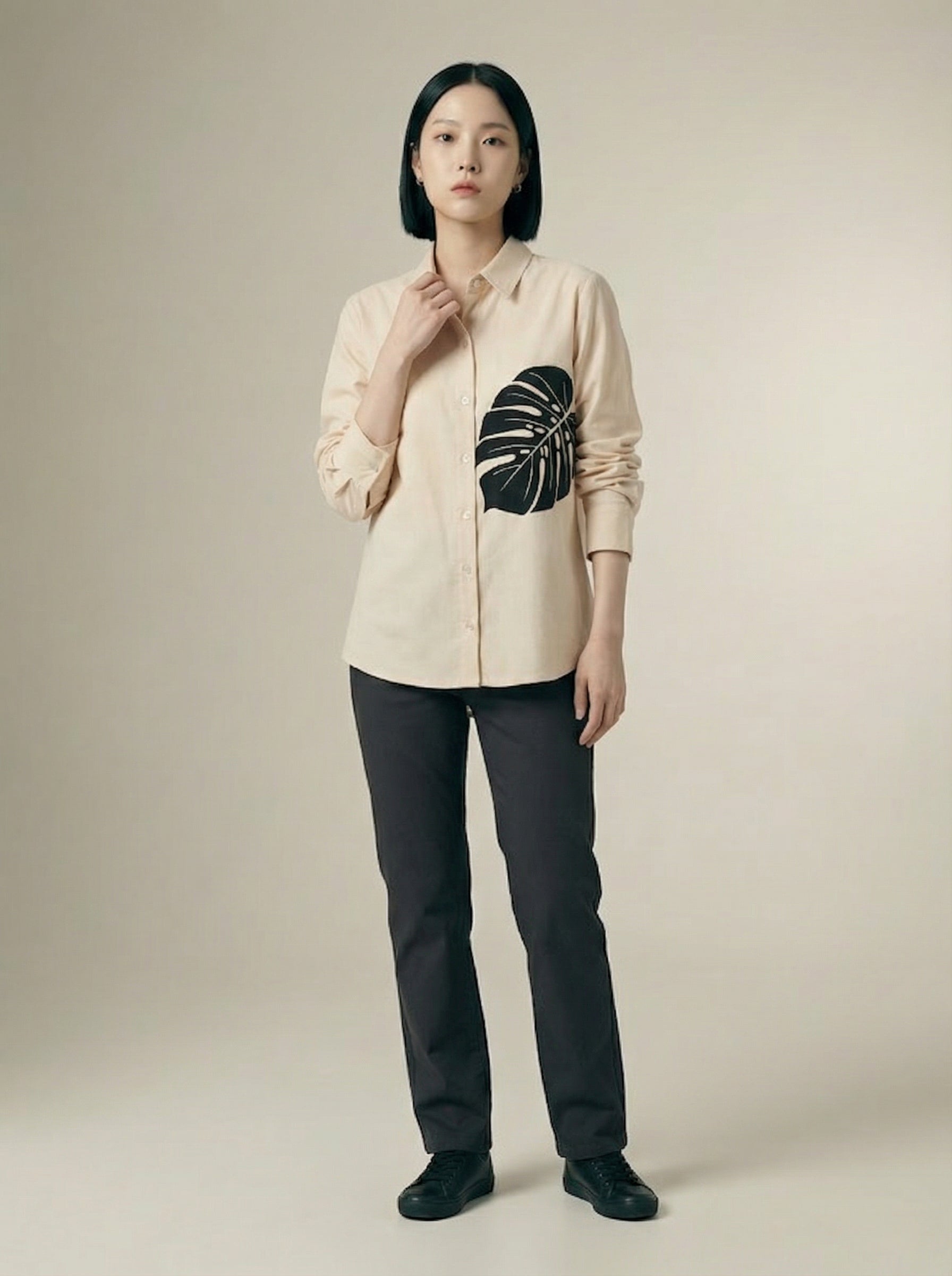 A contemporary cream shirt top featuring a bold black monstera leaf graphic on the front for a clean and artistic statement look. 