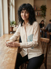 A refined cream shirt top featuring a striking teal ginkgo leaf graphic on the front for a clean artistic look.