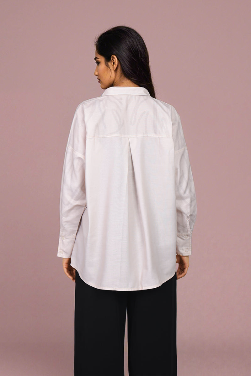 A woman shown from the back wearing a white long-sleeve button-up shirt and black wide-leg pants, standing against a solid dusty pink background.