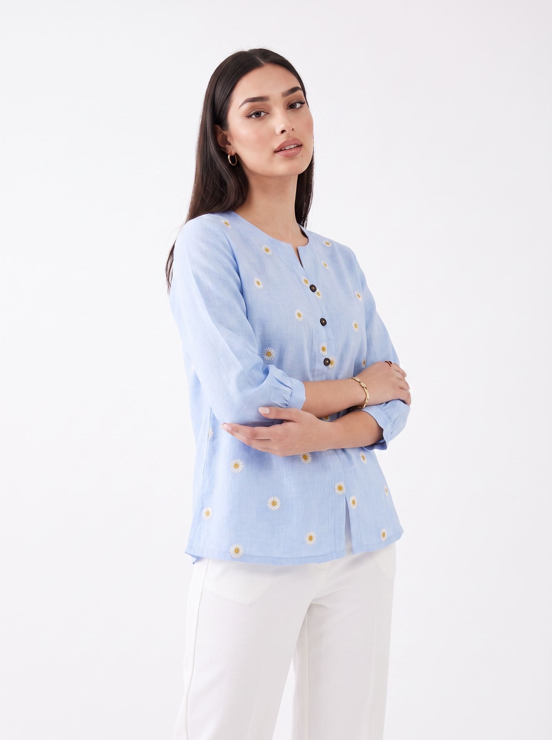 Add a fresh and feminine touch to your everyday wardrobe with this sky blue top, featuring delicate white daisy embroidery with mustard centres scattered across the front, a subtle split neckline, and contrast button detailing