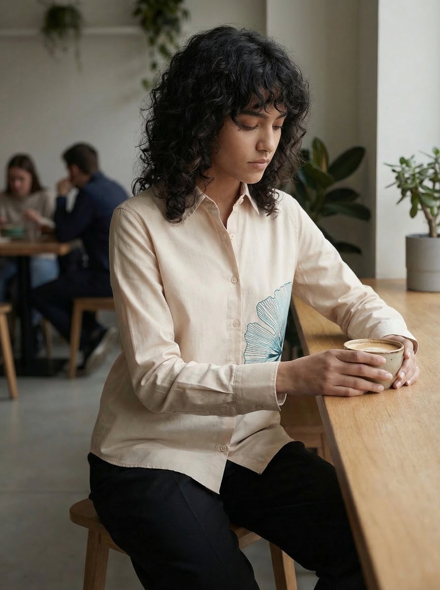 A refined cream shirt top featuring a striking teal ginkgo leaf graphic on the front for a clean artistic look.