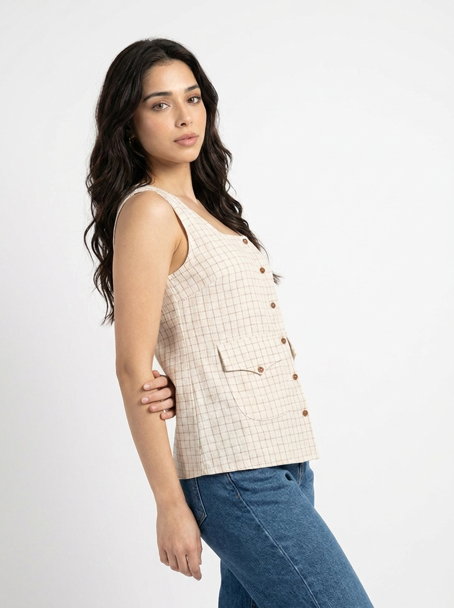 A woman wearing a sleeveless beige and white checkered vest with brown buttons, paired with blue jeans, photographed against a plain white studio background.