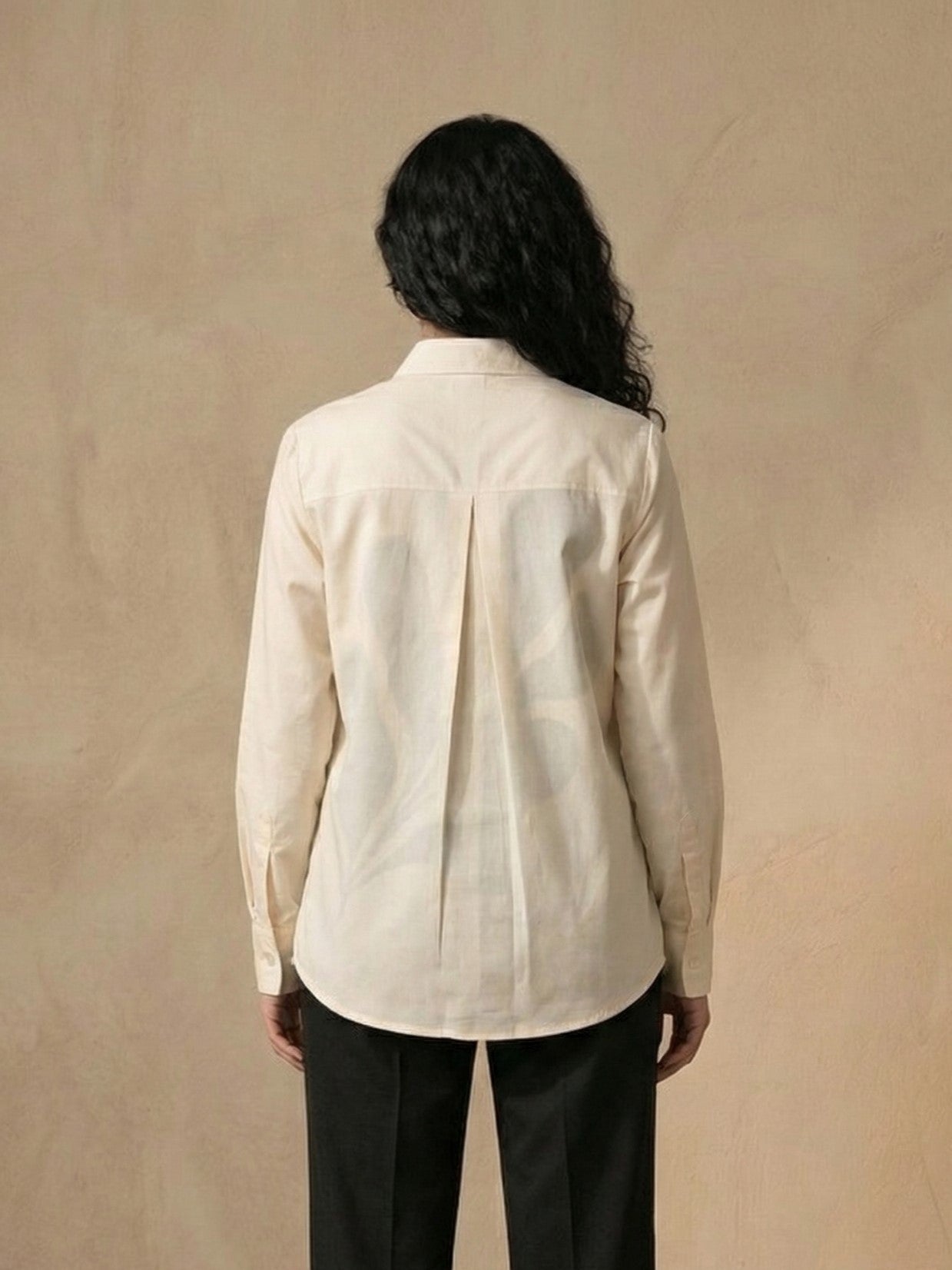 A person shown from the back wearing a light cream-colored long-sleeve button-up shirt and black pants, standing against a textured beige background.