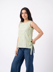 Add a soft feminine touch to your wardrobe with this sage green sleeveless top, featuring delicate multicolor floral embroidery scattered across the front, a clean round neckline, and stylish side tie-up detailing. 