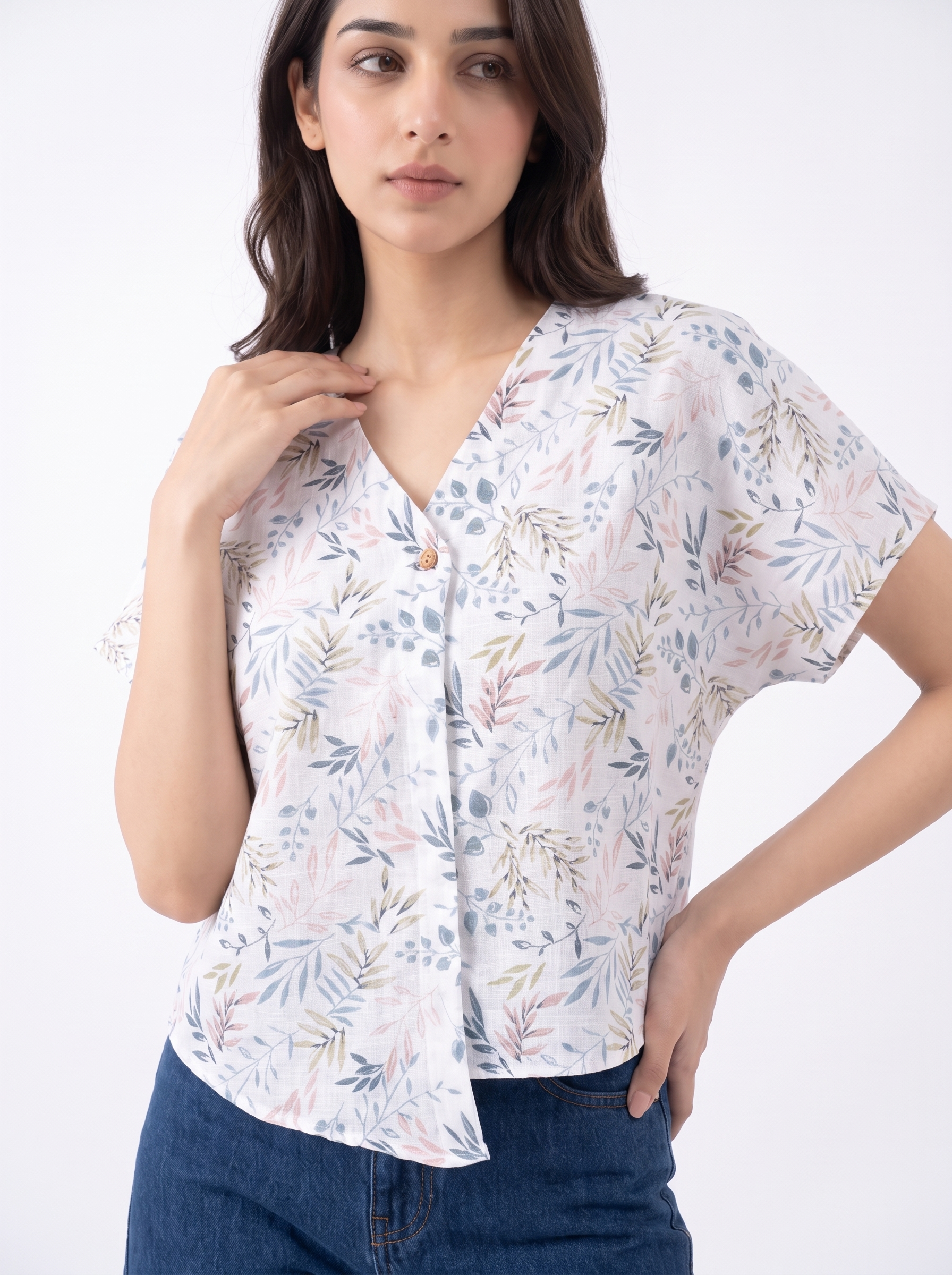 A woman wearing a white short-sleeve button-up blouse with a delicate pastel botanical print in pink, blue, and green, paired with dark blue jeans, set against a plain white studio background.