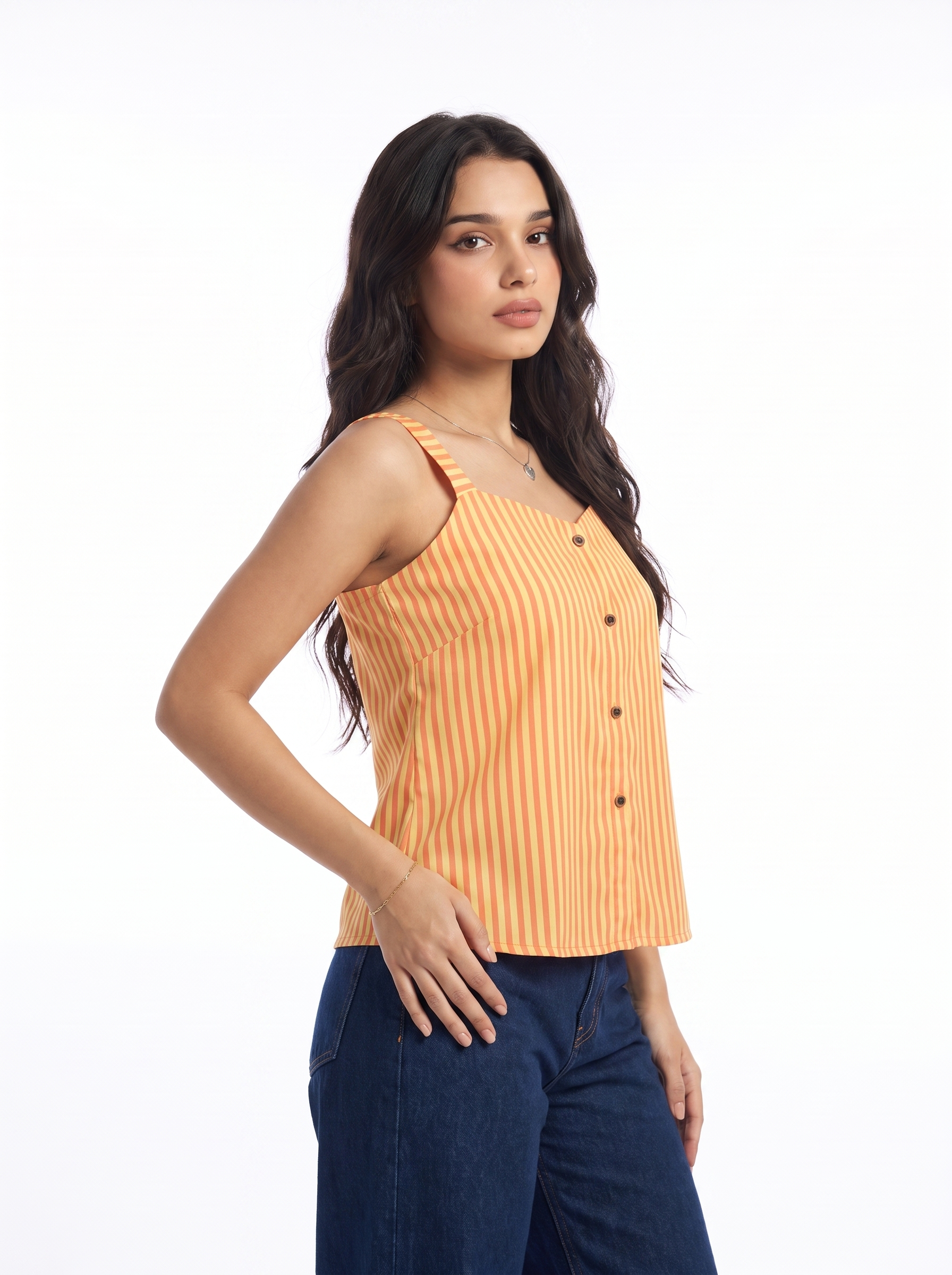 A woman modeling a sleeveless orange and white vertically striped button-up top with dark blue jeans, photographed against a solid white studio background.