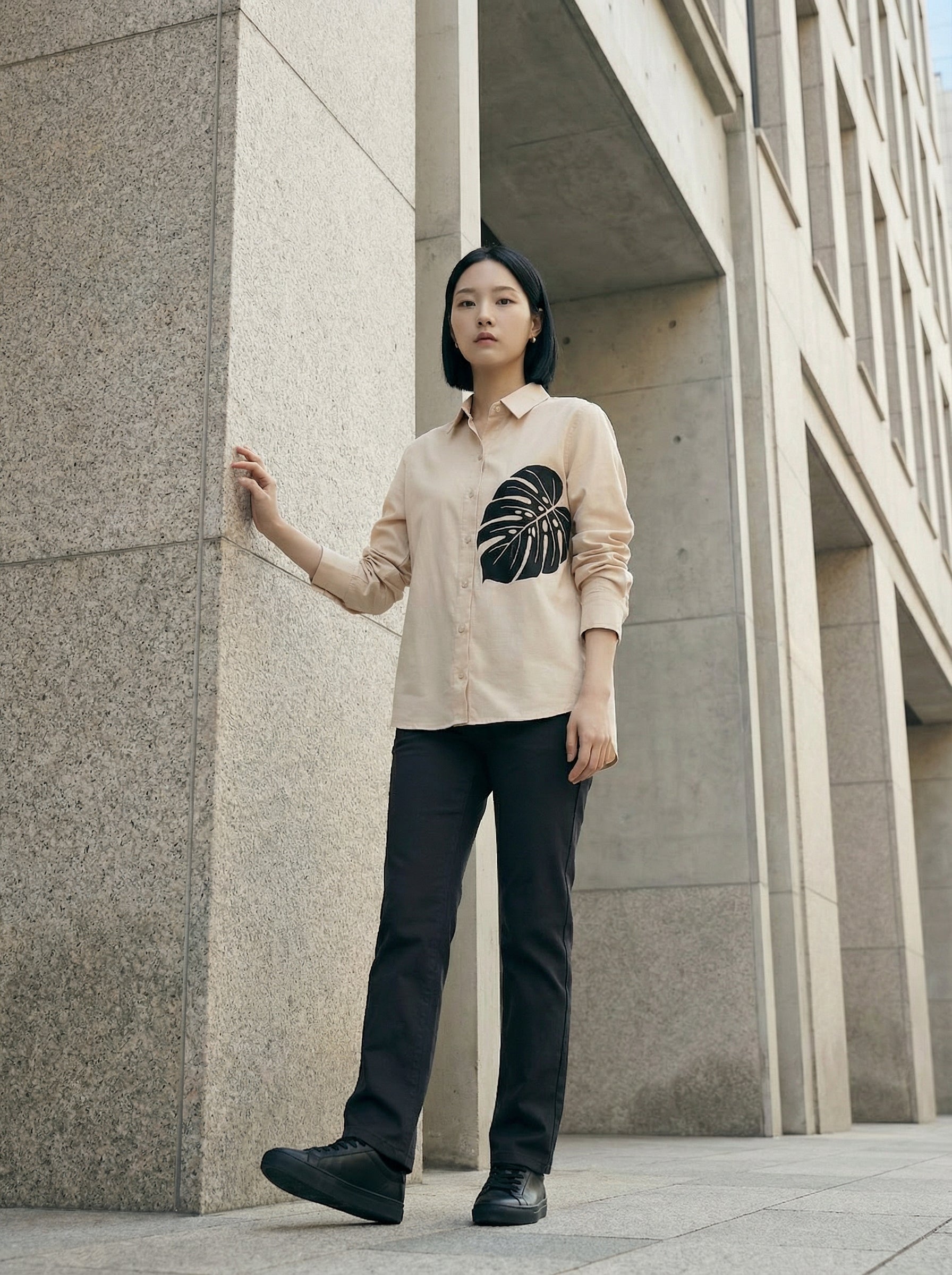 A contemporary cream shirt top featuring a bold black monstera leaf graphic on the front for a clean and artistic statement look. 