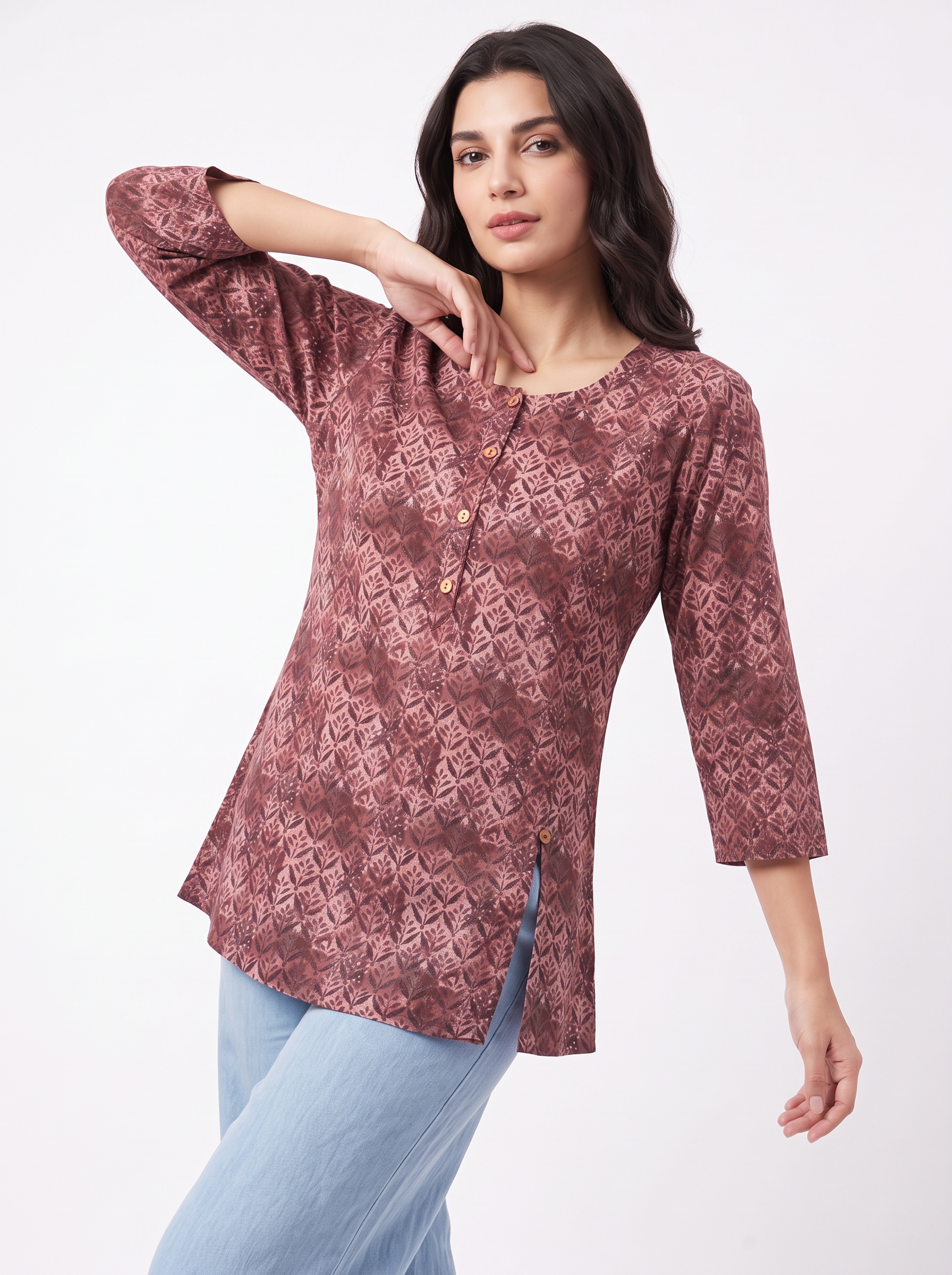 A woman modeling a three-quarter sleeve tunic top with a dusty rose and brown geometric pattern, paired with light blue jeans, against a plain white background.