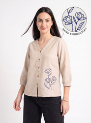 A woman modeling a beige linen button-up shirt with a V-neck and blue floral embroidery on the lower front. The image features a 'HAND EMBROIDERY' graphic overlay in the top right corner, set against a clean white background.