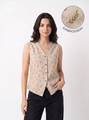A woman modeling a sleeveless beige vest with a subtle embroidered pattern, paired with black pants, against a plain white background. An inset circle in the top right highlights the embroidery detail with the text 'EMBROIDERY'.