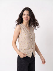 A woman modeling a sleeveless beige linen vest with a yellow and pink feather pattern, paired with black pants, against a plain white studio background.