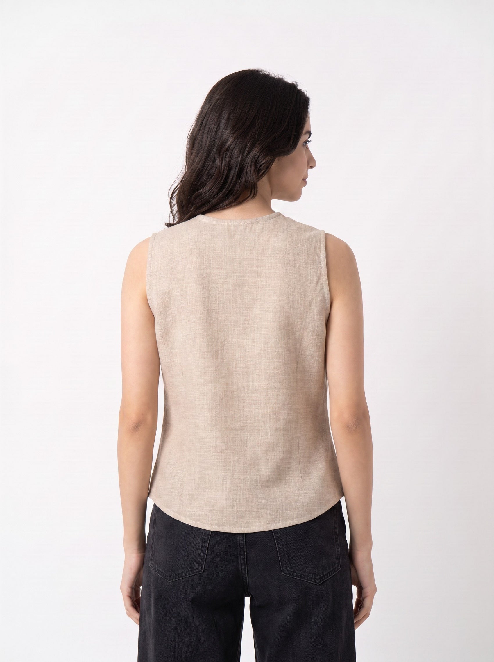 A woman shown from the back wearing a sleeveless beige linen top and dark charcoal pants against a plain white studio background.