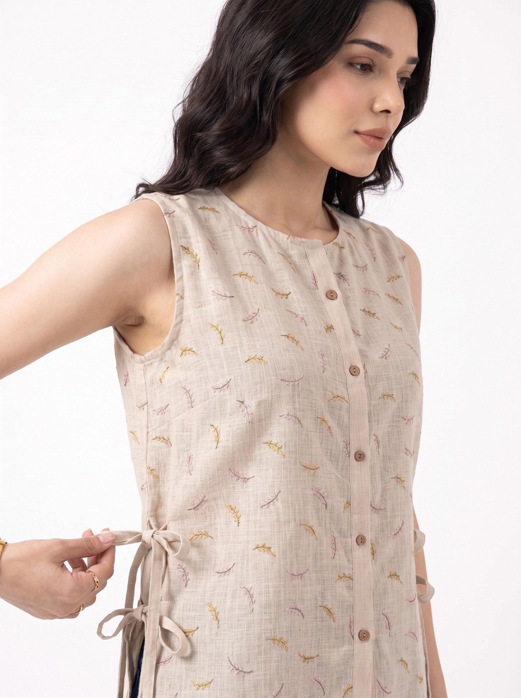 A woman wearing a sleeveless beige linen-look top with a small multicolor leaf print and button front, shown against a plain white background.