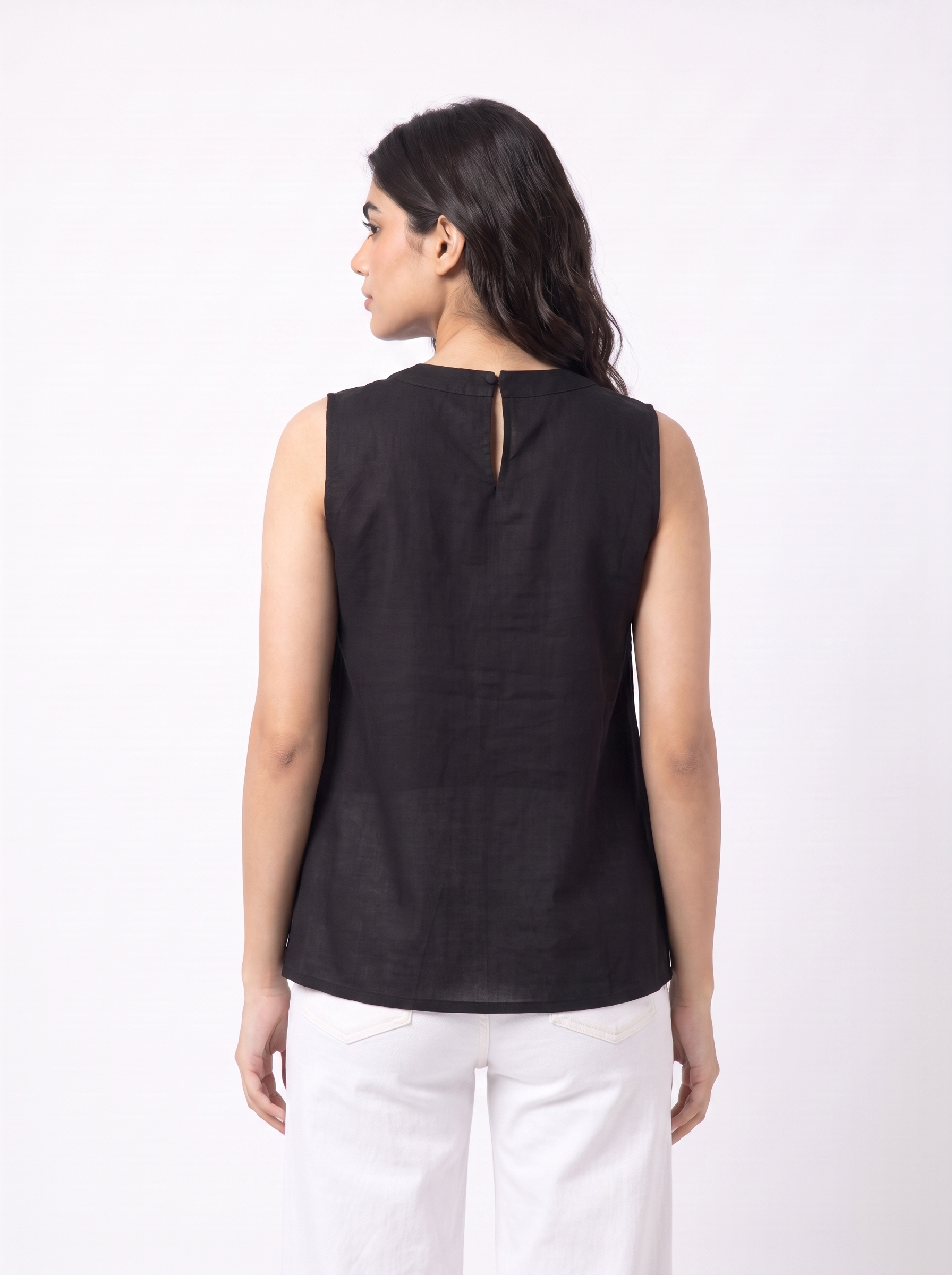 A woman shown from the back wearing a sleeveless black top and white pants against a plain white studio background.