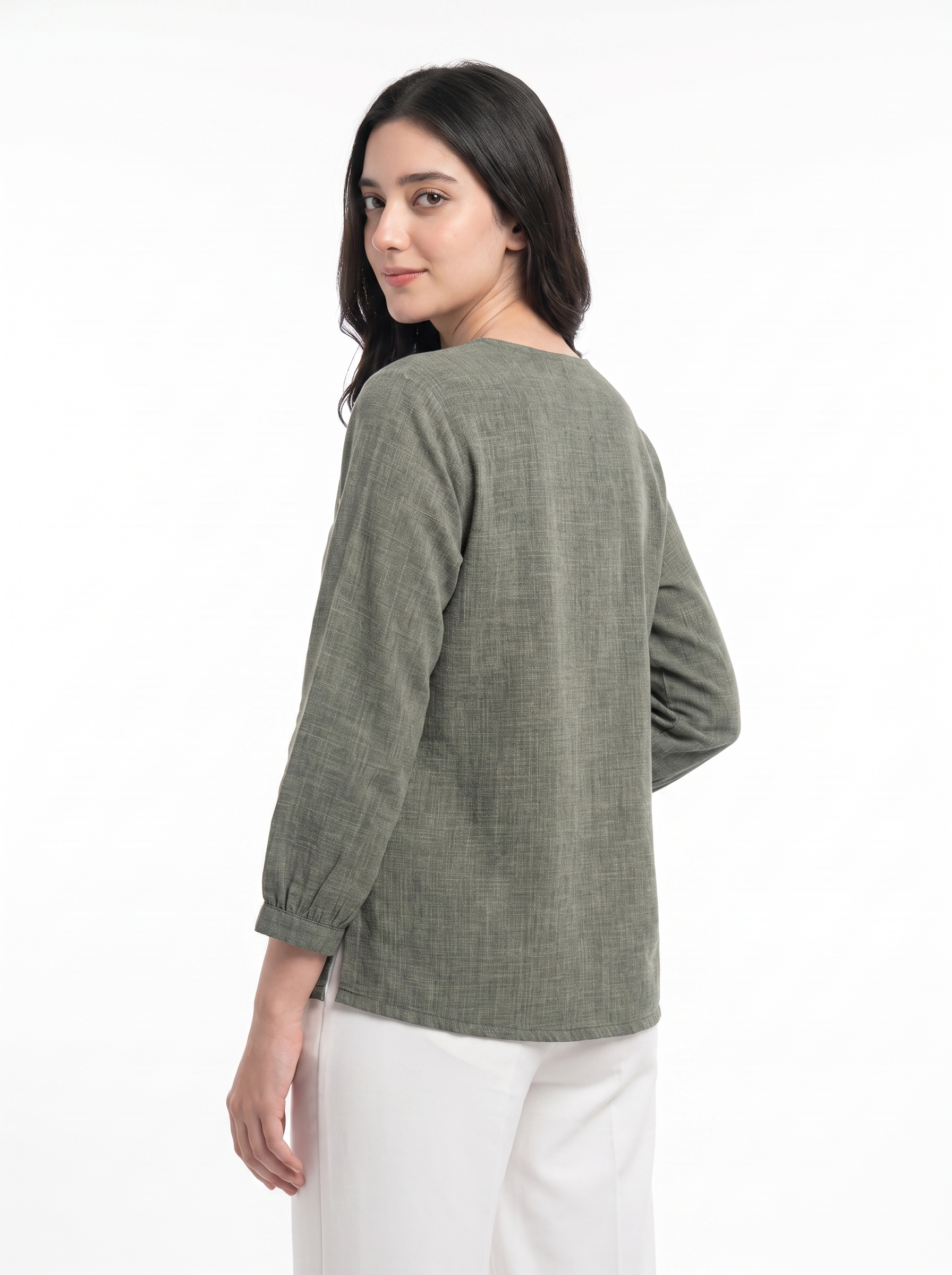 A woman wearing a textured sage green long-sleeve top and white pants, photographed from the back against a plain white studio background.