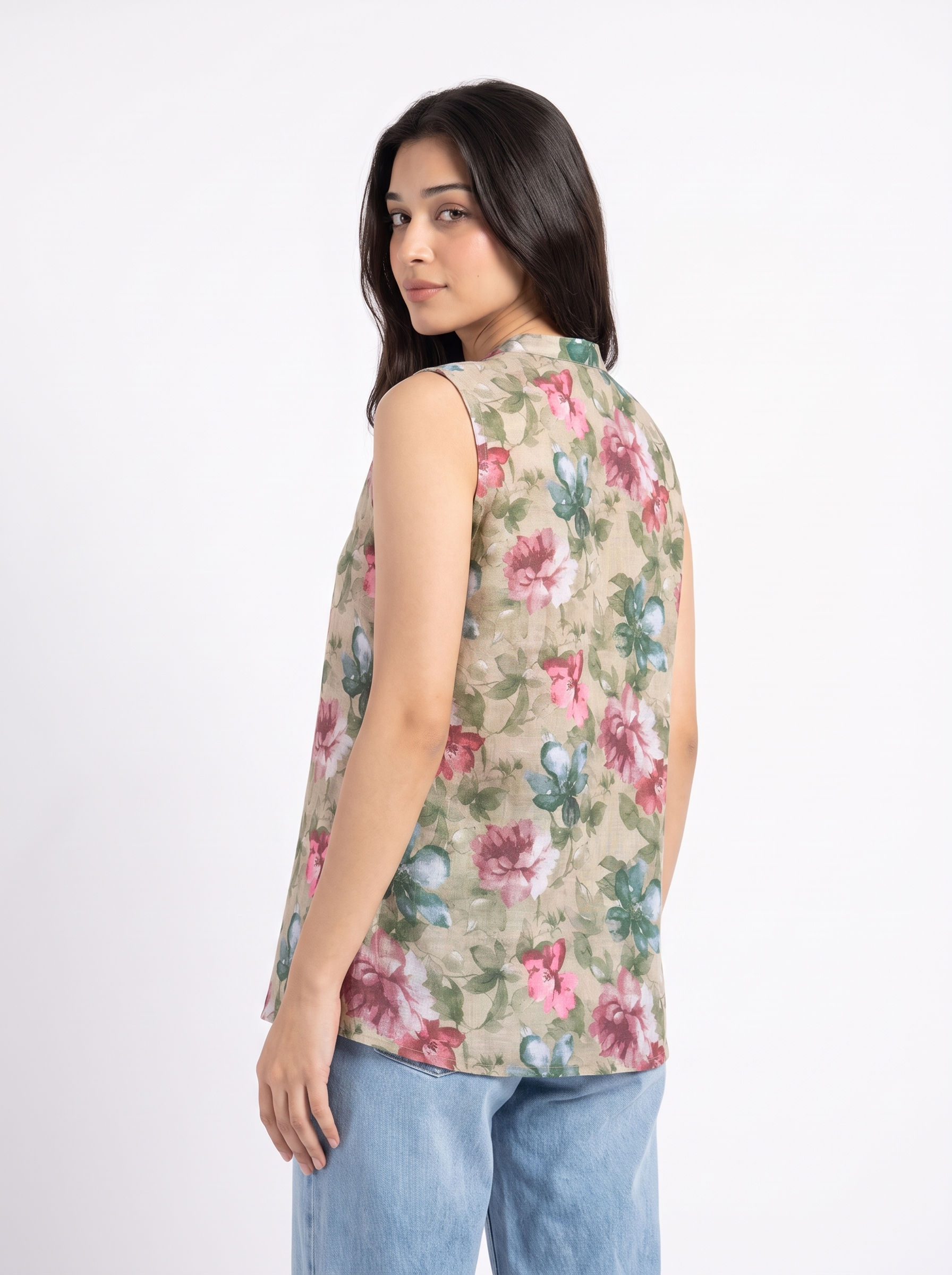 A woman wearing a sleeveless beige top with a pink and green floral print, paired with light blue jeans, photographed against a plain white background.